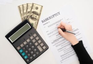 A person signing bankruptcy paperwork with a calculator and money on the desk in British Columbia